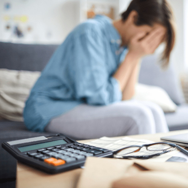 woman with hand to her face in the background in front calculator, papers and laptop.