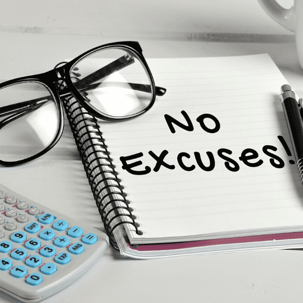 No excuses word written on a notebook page next to a calculator and black frame glasses.