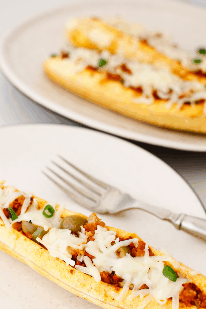 Close-up of stuffed baked plantains (canoas de plátanos maduros) filled with seasoned ground beef, olives, melted cheese, and green onions on a plate