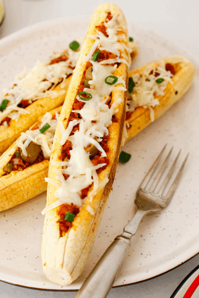 Stuffed baked plantains (canoas de plátanos maduros) filled with seasoned ground beef, olives, melted cheese, and green onions on a plate