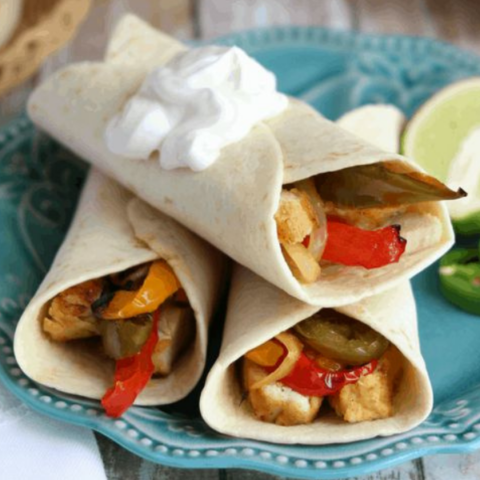 Sous Vide Tequila-Lime Chicken Fajitas wrapped in tortillas with sautéed peppers and onions, topped with sour cream on a turquoise plate.