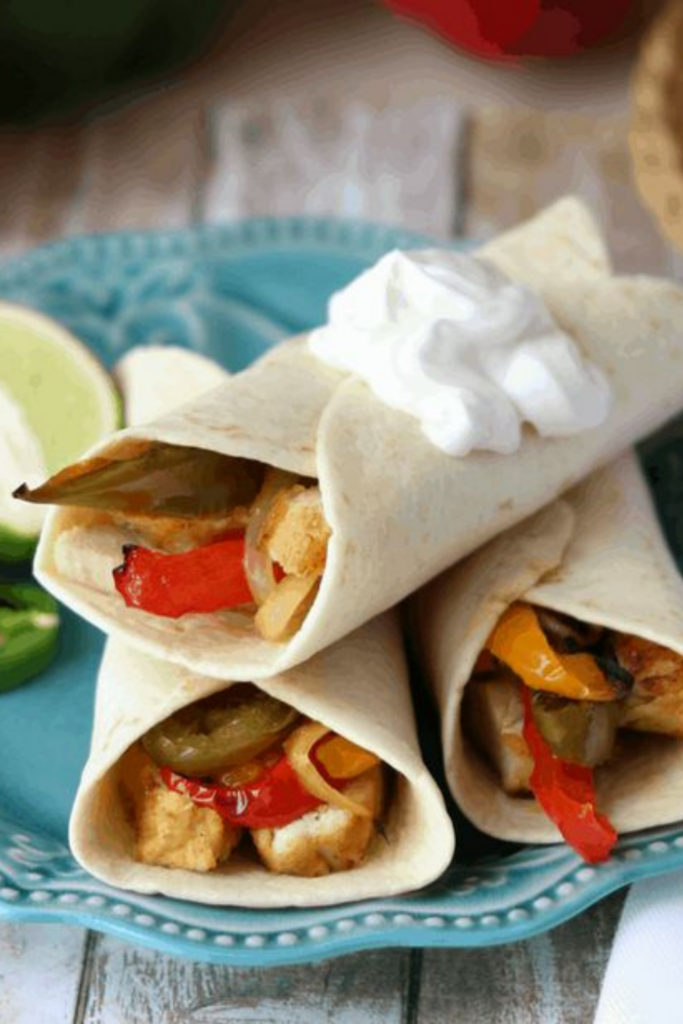Plated Sous Vide Tequila-Lime Chicken Fajitas arranged with sour cream on top and surrounded by fresh lime and pepper slices.