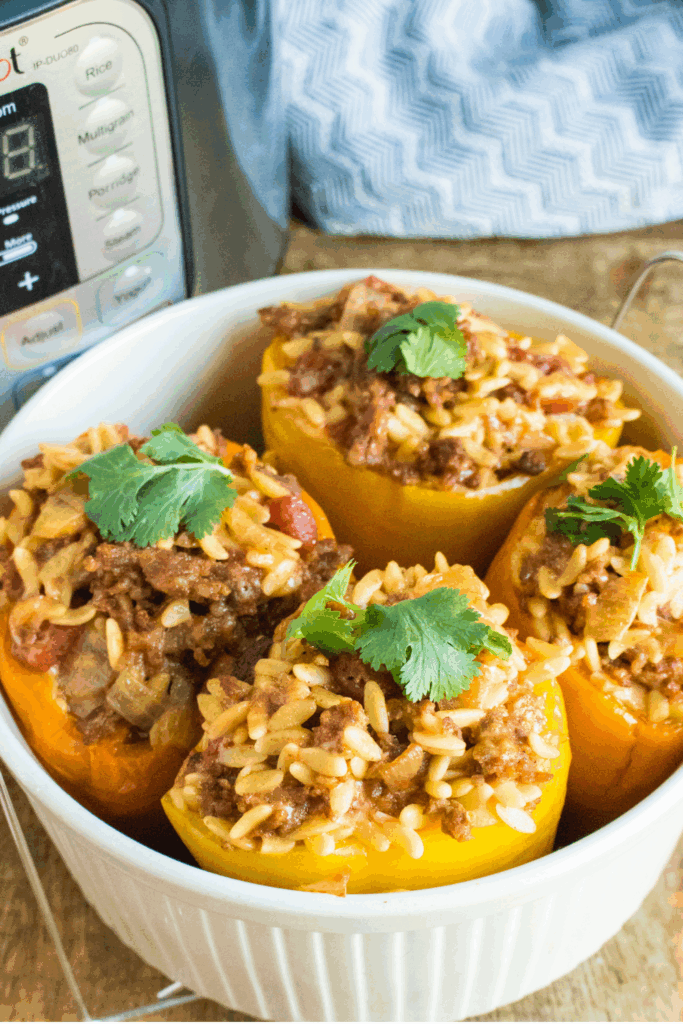 Instant Pot stuffed peppers filled with Italian sausage and orzo, served in a white baking dish and topped with fresh herbs, showing a hearty pressure cooker dinner ready to serve.