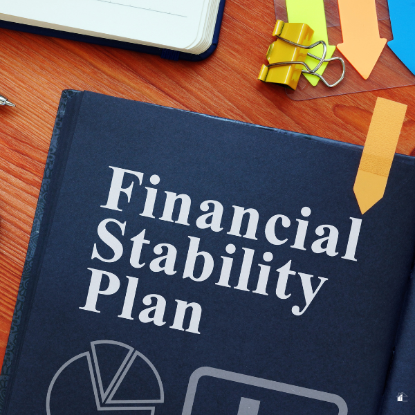 Black book titled, Financial Stability Plan, with charts and pens near it.