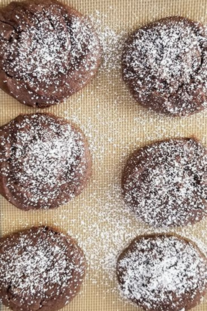 Sea Salt & Caramel Nutella Cookies freshly baked and cooling on a silicone baking mat, topped with powdered sugar.