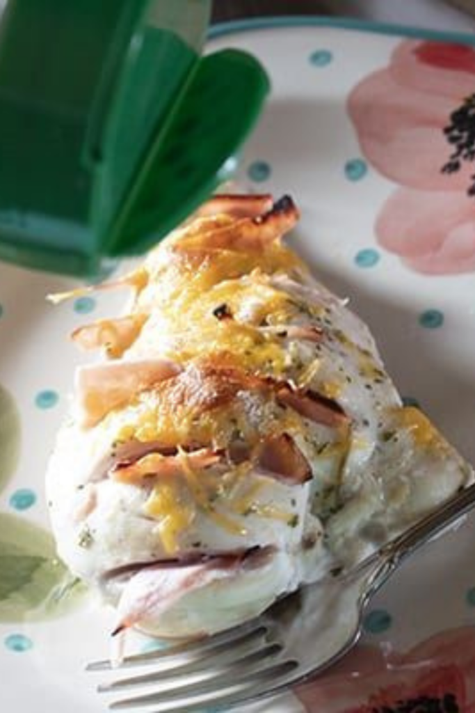 Close-up of finished Ranch Hasselback chicken breast on a floral plate, showing golden melted cheese and visible ham slices.