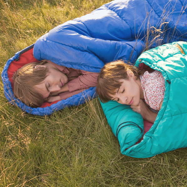 Couple sleeping in sleeping bags in a field.
