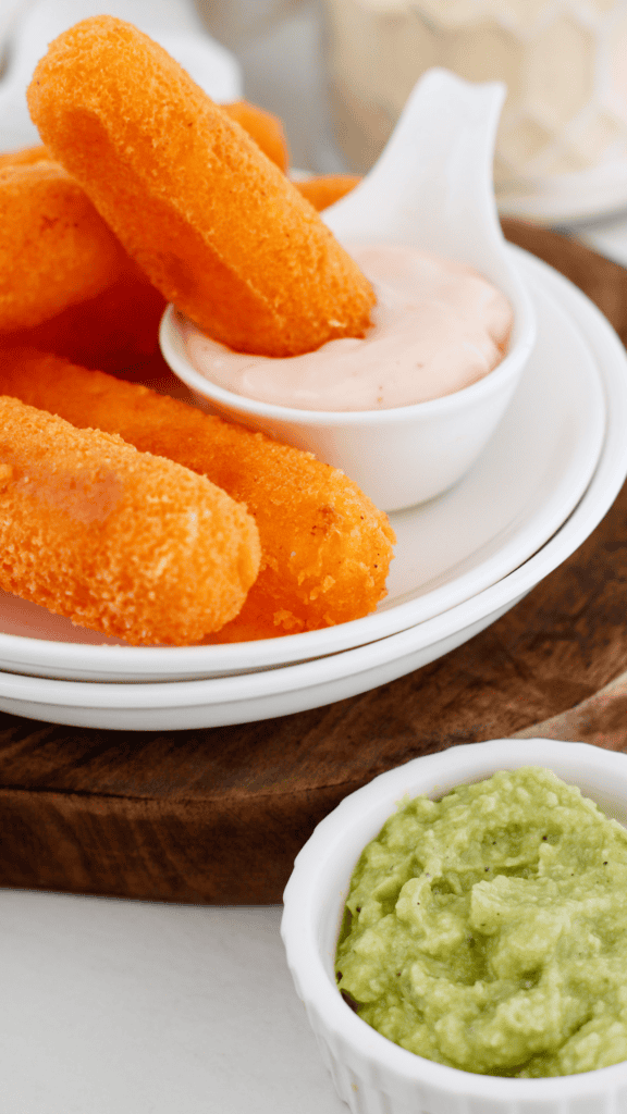 Golden Puerto Rican sorullos served on a white plate with creamy dipping sauce and fresh guacamole on the side.