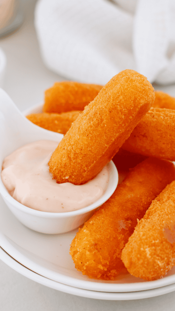 Crispy golden Puerto Rican sorullos arranged on a white plate with one cornmeal fritter resting in creamy dipping sauce.