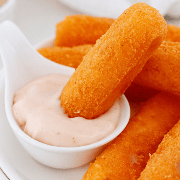 Crispy golden Puerto Rican sorullos arranged on a white plate with one cornmeal fritter resting in creamy dipping sauce.