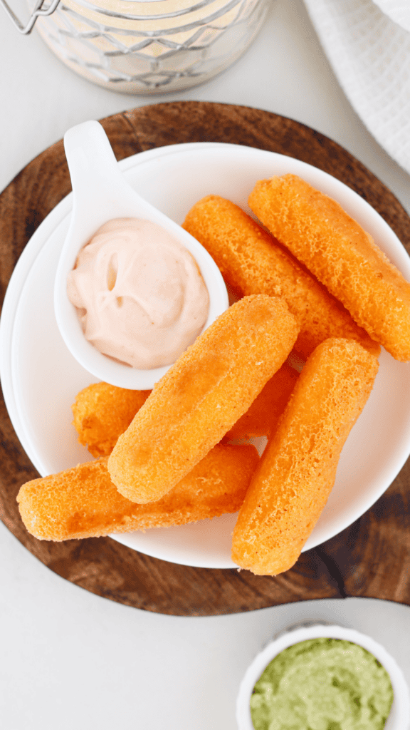 Plate of golden Puerto Rican sorullos served with creamy dipping sauce and a small bowl of guacamole.