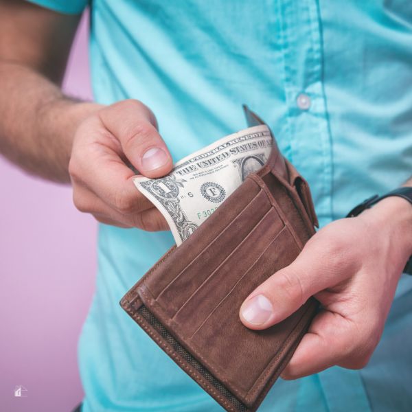 A man holding a brown wallet and pulling a dollar bill.