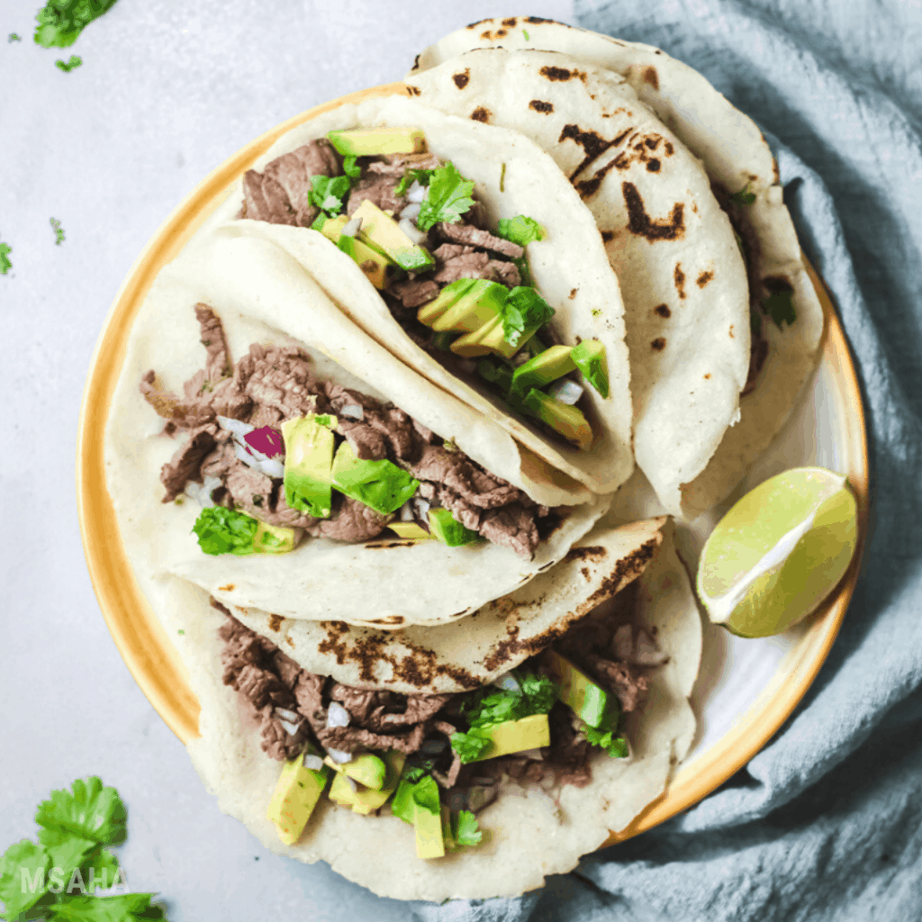 steak tacos on plate with lime wedge on the side