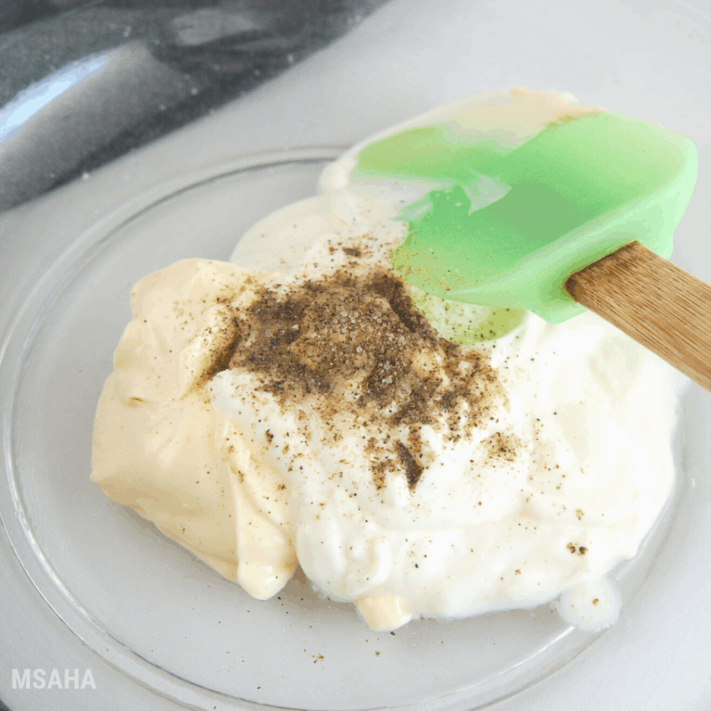 A mayonnaise, Mexican sour cream, salt, and pepper combined in a glass bowl.