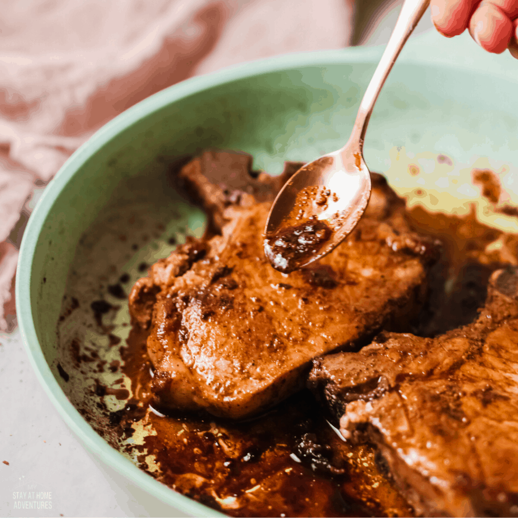 pork chops in pan with a spoon over them.