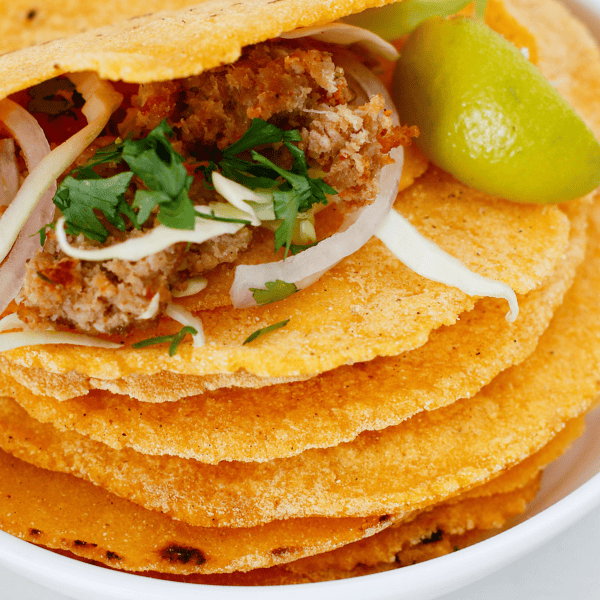 A homemade corn tortilla is filled with seasoned meat, shredded cabbage, onion, and cilantro, with a fresh lime wedge beside it.