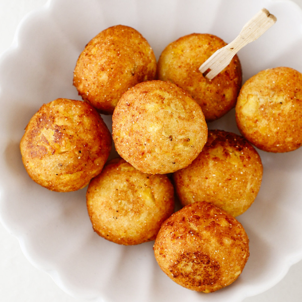 Fried Bolitas de Plátano with golden crust served in a scalloped white bowl.