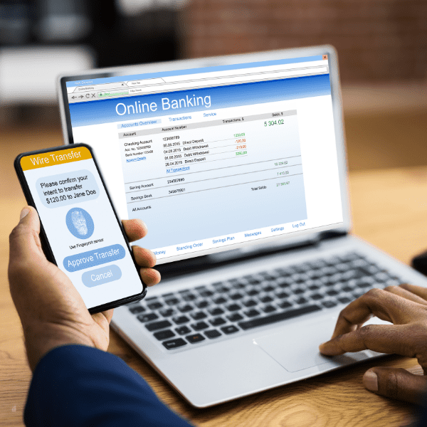 man holding a phone and a laptop accessing online banking.