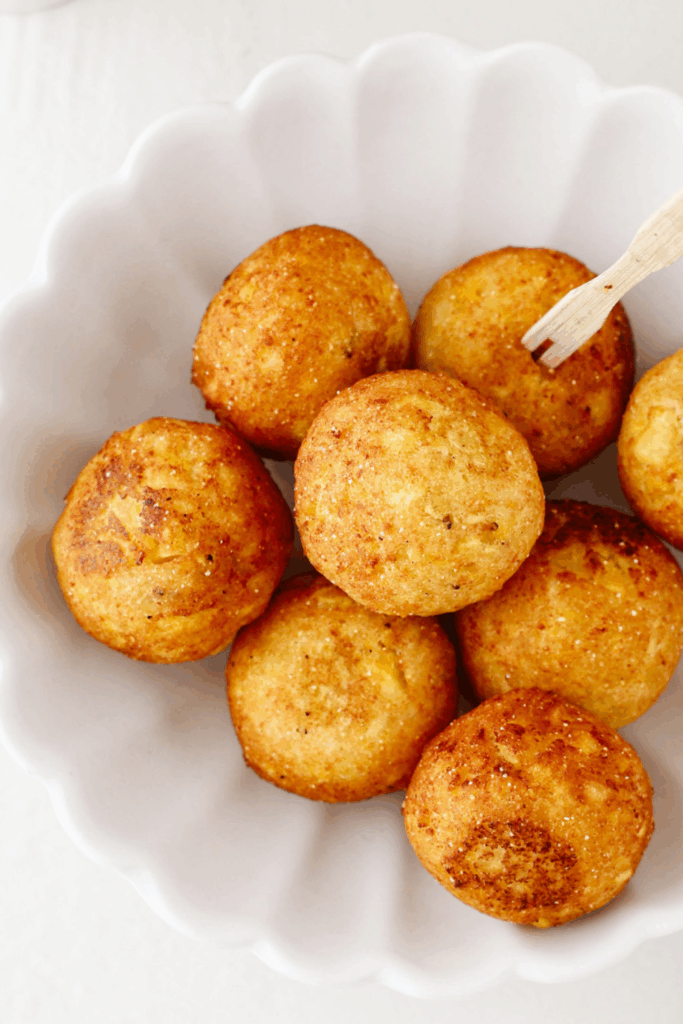 Fried Bolitas de Plátano with golden crust served in a scalloped white bowl.