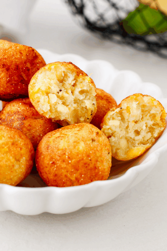 Crispy plantain balls with soft, fluffy insides on display in a white dish.