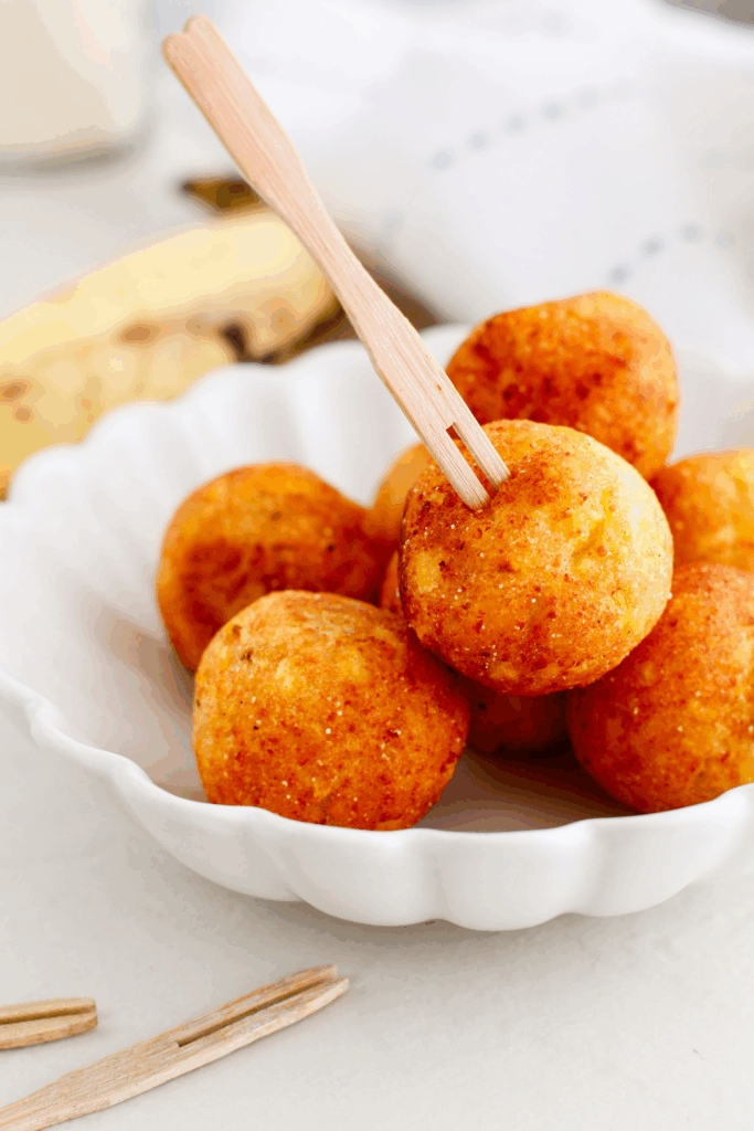 One golden plantain ball lifted from a bowl of freshly fried Bolitas de Plátano.