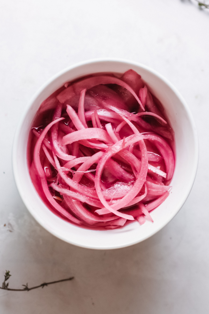 Top-down view of quick pickled red onions in a white bowl showing crisp texture and rich pink color.