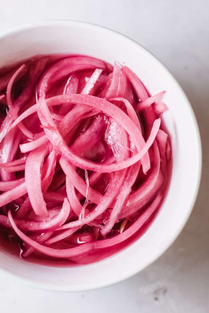 Close-up of glossy sliced red onions marinating in tangy vinegar brine for a quick pickled onions recipe.