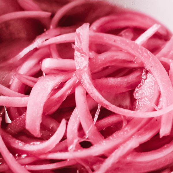 Close up of red picked onions in a white container.