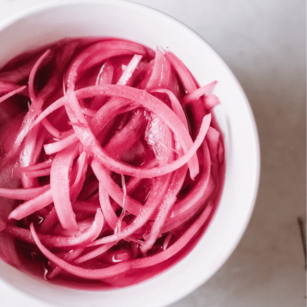 Close up of sliced picked onions on a white bowl.