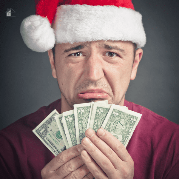 A man wearing a Santa hat looks distressed while holding a few dollar bills, symbolizing the financial stress of overspending during the Christmas season.