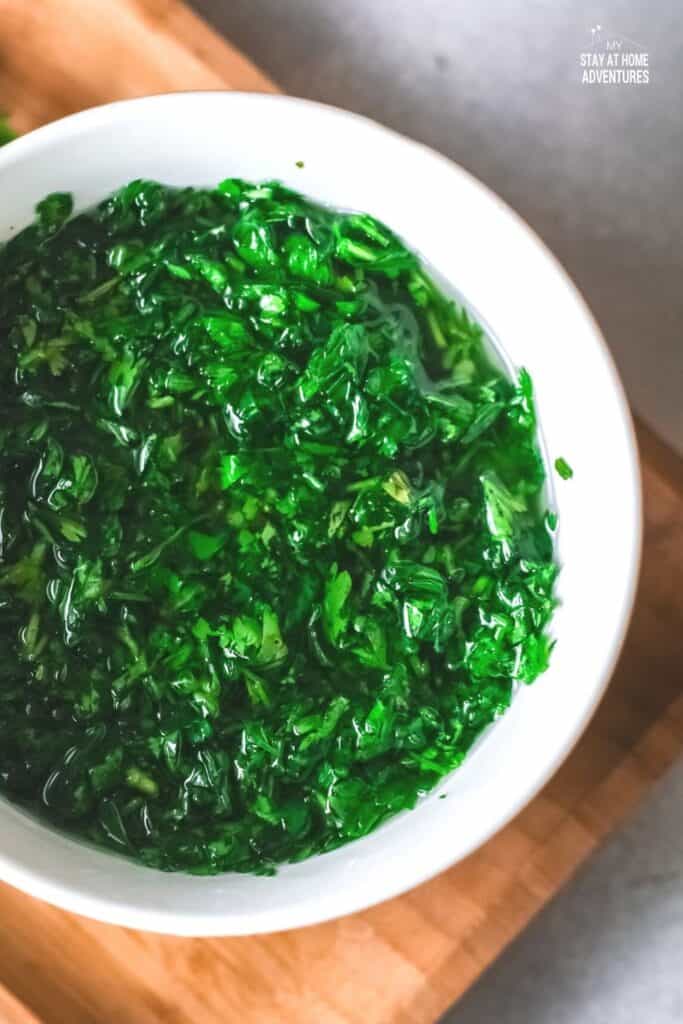 green chimichurri plated in white plate on top of wooden board.