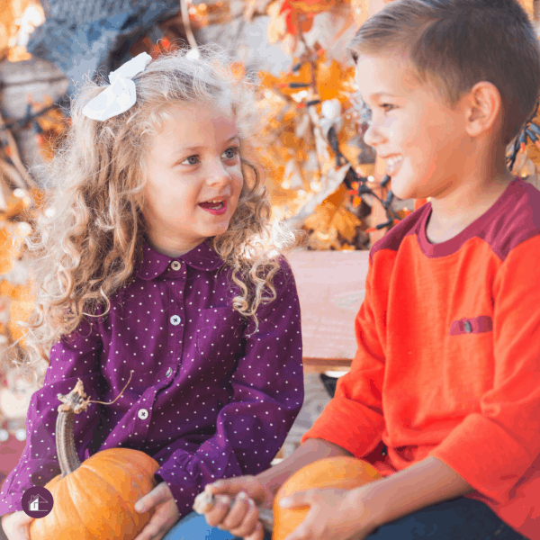 two children sitting on a bench holding pumpkins