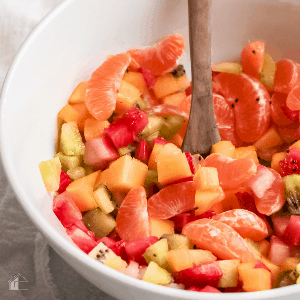 photo of fruit in a white bowl and wooden spoon