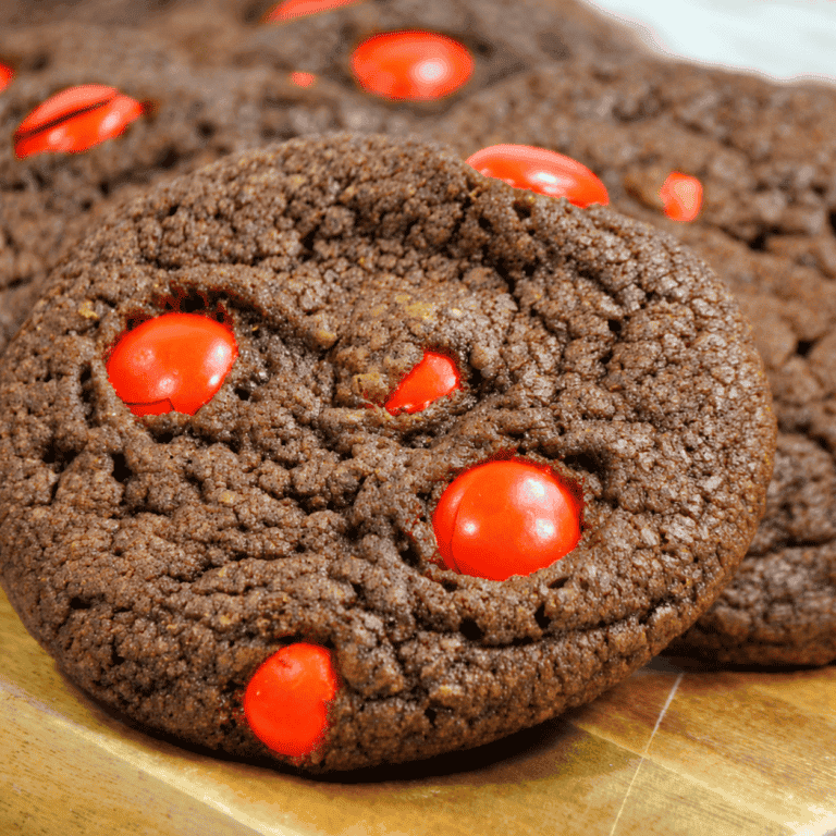 A large Nutella cookie filled with orange candies rests in front of overlapping cookies on a wooden board.