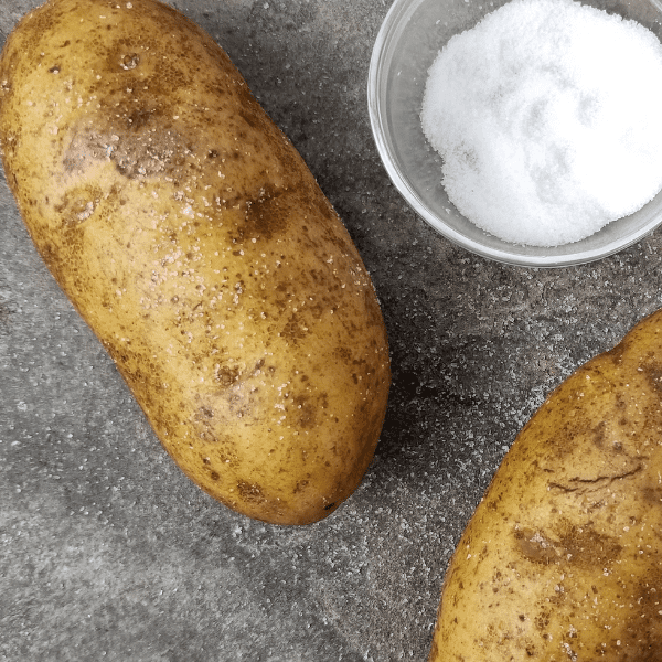 photo of two potatoes covered with salt and a small dish full of salt.
