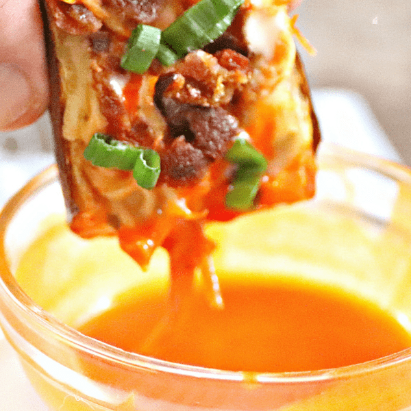 buffalo chicken potato skin being dipped in hot sauce.