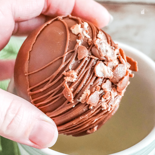 Female hand holding a whopper hot cocoa bomb above a mug.