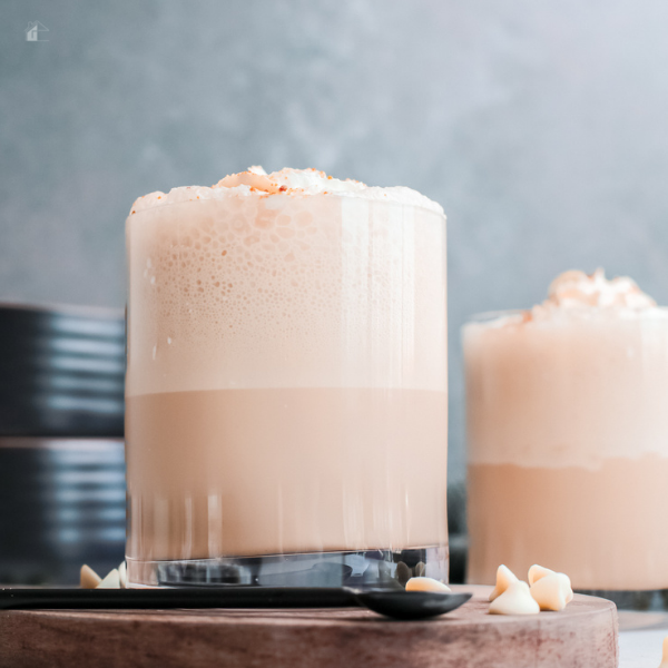 Two mugs of White Chocolate Frappuccino. the mug in front is on top of a board.