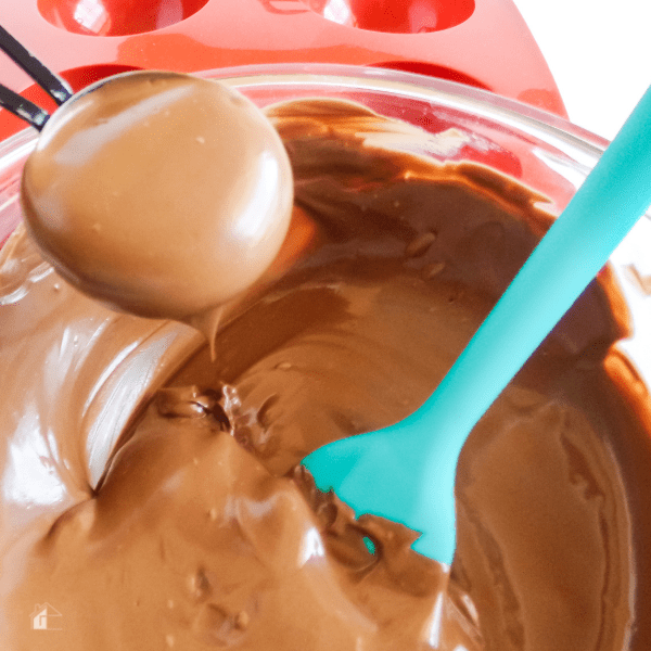 melted chocolate being scooped from bowl. a teal color spatula inside the bowl.