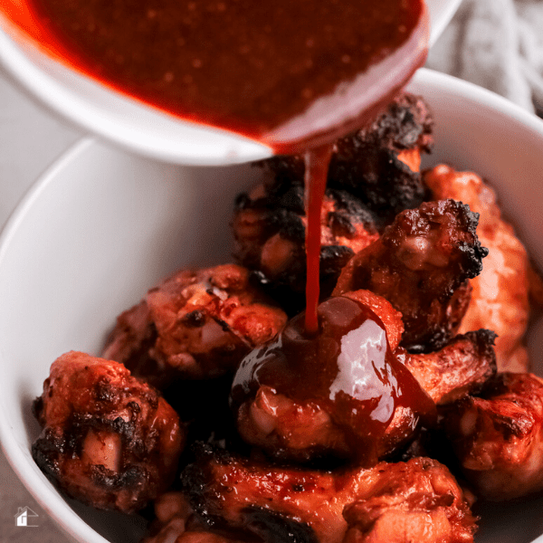 female hand pouring sauce over cooked chicken wings.

