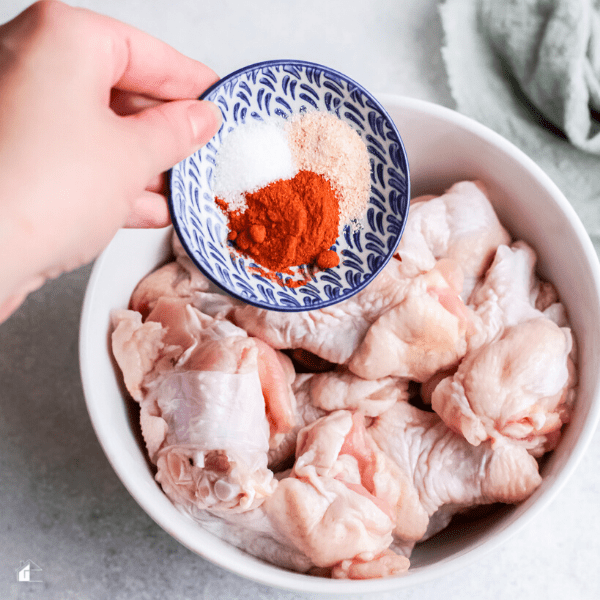 women hands about to add season to a bowl full of wings.
