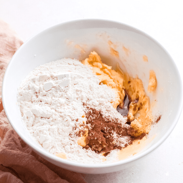 Creamed sugar, vanilla extract, cinnamon, and flour in a white mixing bowl.