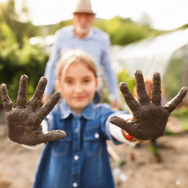 Girl gardening with her grandfather holding muddy hands.