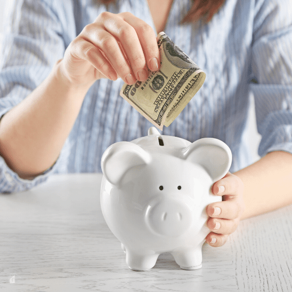 Female hand putting $100 bill into a white piggy bank.