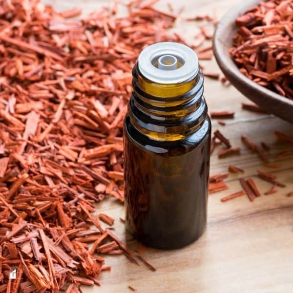 A bottle of sandalwood essential oil on a wooden table, with sandalwood chips in the background.