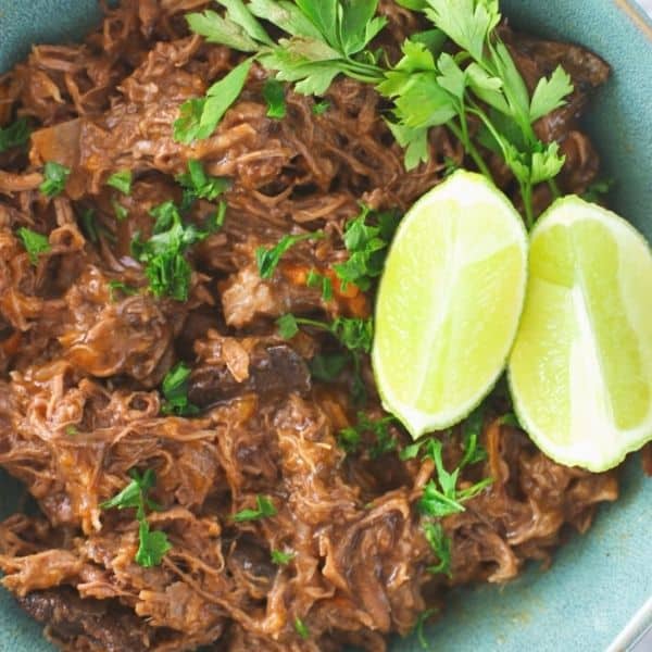 Carne Mechada Chelana plated and garnished with cilantro and limes.