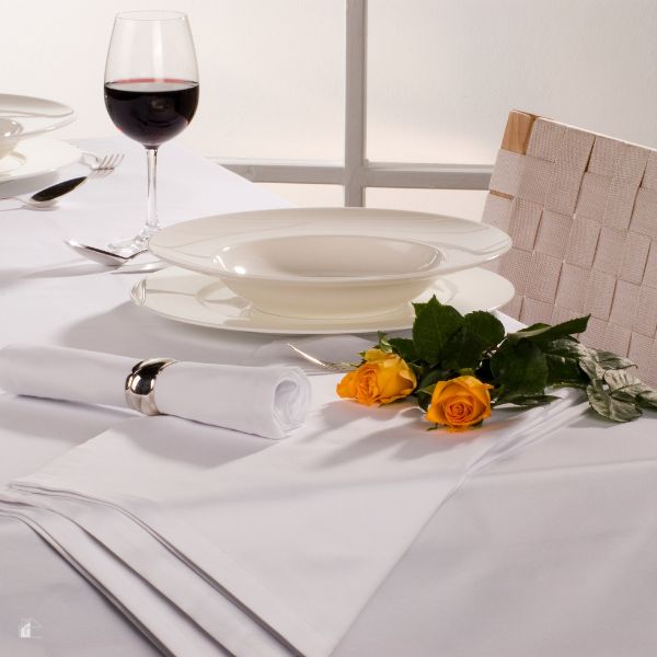 White cloth table with white napkin and yellow roses on the table.