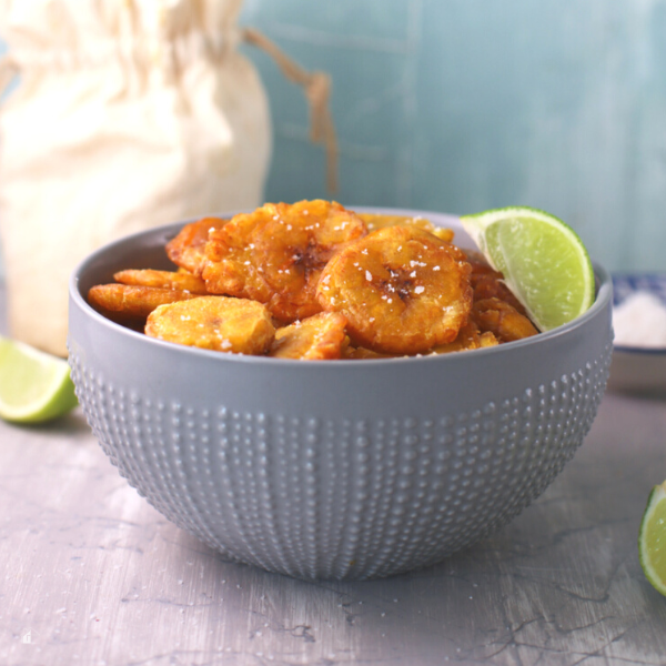Side photo of tostones in a grey bowl with a lime on the top.