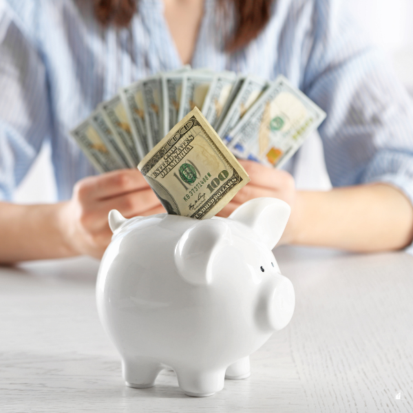 Woman sitting holding cash and a piggy bank close up.