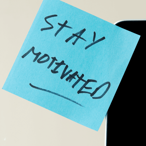 Blue post-it with handwritten text, stay motivated.